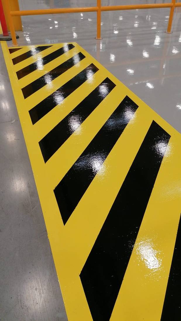 Señalética de seguridad sobre piso epóxico en zona de máquinas